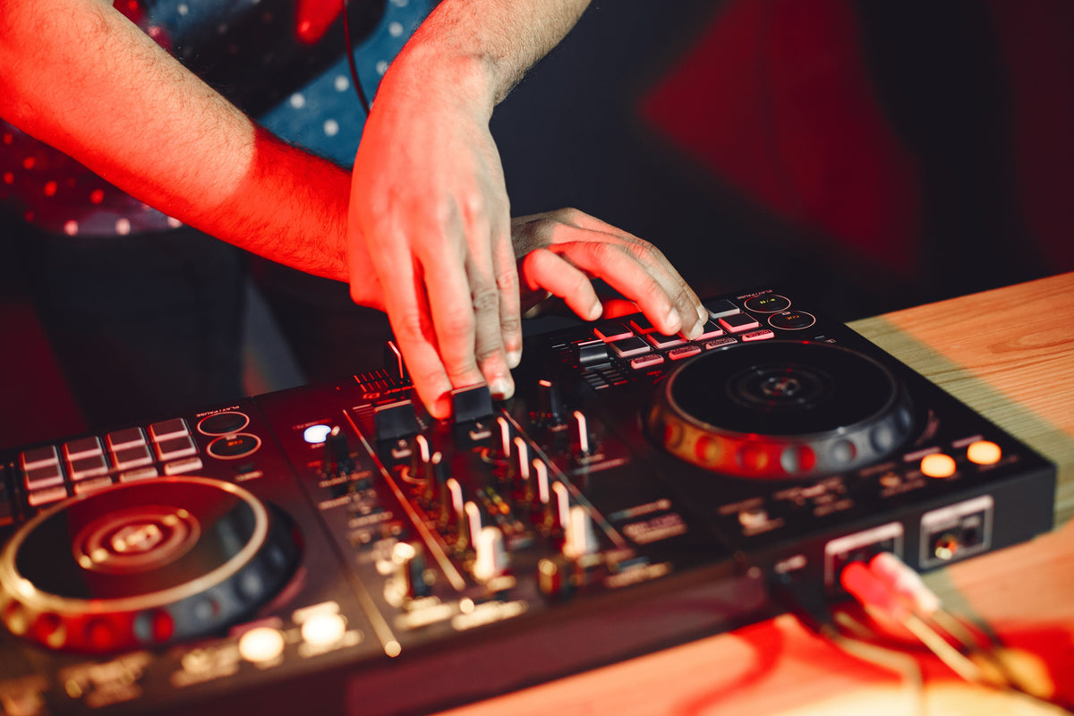 Hands adjusting a DJ controller with two decks under red lighting.